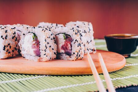 Close up of tasty sushi-rolls on on wooden board with soy sauce and chopsticks on decorative bamboo napkin.の写真素材