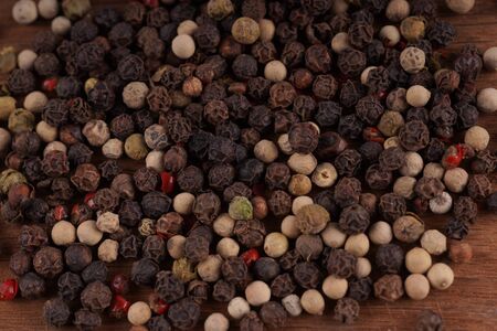 Close up of condiment on brown wooden background. Bunch of different peppers on table with space for...