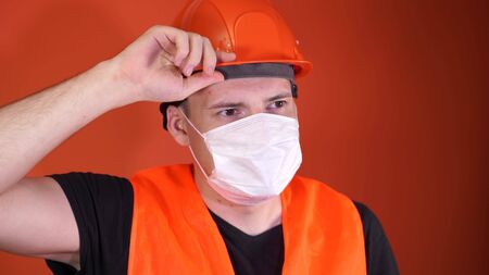 Portrait of young man in medical mask on his face on orange background. Adult male covered face with...