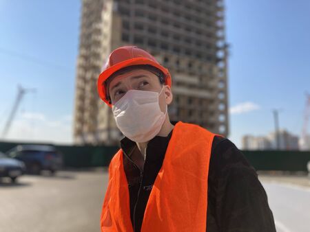 Portrait of male construction worker in medical mask and overalls on background of house under...