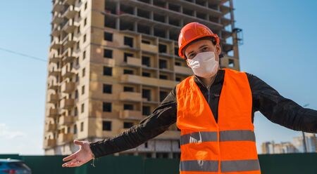Portrait of male construction worker in medical mask and overalls on background of house under...