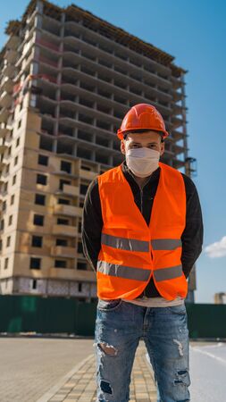 Portrait of male construction worker in medical mask and overalls on background of house under construction.の写真素材