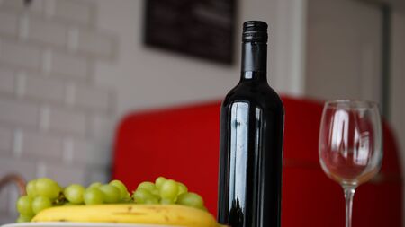 Close up of open bottle of wine and glass of wine with fruits on plate on table in kitchen.の写真素材