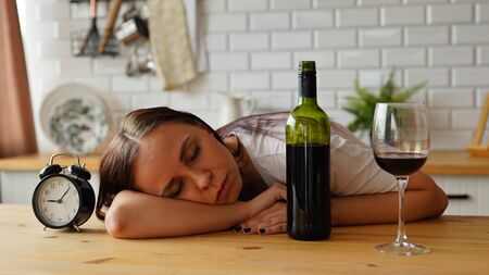 An alcoholic woman sleeps in the kitchen in the morning, near a bottle of wine. Concept: Hangoverの写真素材