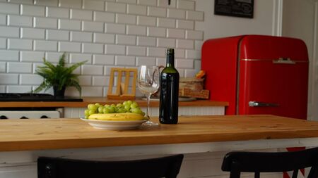 Close up of open bottle of wine and glass of wine with fruits on plate on table in kitchen.の写真素材