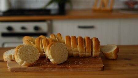 Chopped white bread on wooden board on kitchen table.