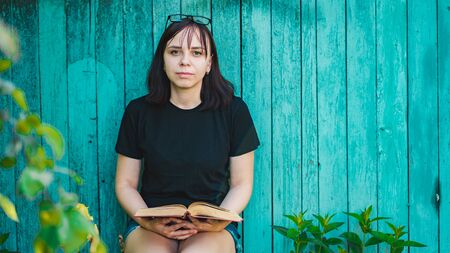 Close up of young woman with book on background of old wooden house.の写真素材