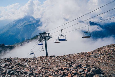 Clouds enveloping modern ropeway with benches in amazing mountainous terrain.の写真素材
