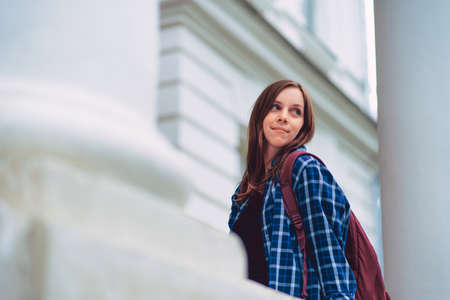 Low angle of young woman with backpack looking away over shoulder while standing on porch of...