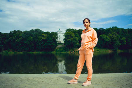 Female tourist standing and looking at camera on blurred background of pond and estate.
