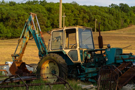 Weathered excavator digging ground during agricultural works in field on summer day in countrysideの写真素材