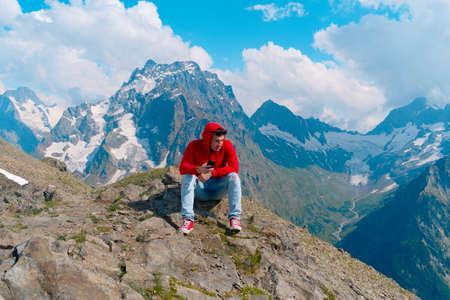 Male traveler using mobile phone against cloudy sky on sunny day in mountainous terrainの写真素材