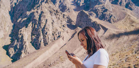 Young woman browsing mobile phone, standing in hilly area. Female traveler stands with smartphone on...