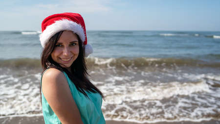 Woman celebrating Christmas near sea. Delighted female in Christmas hat smiling while standing near waving sea on resort.の写真素材