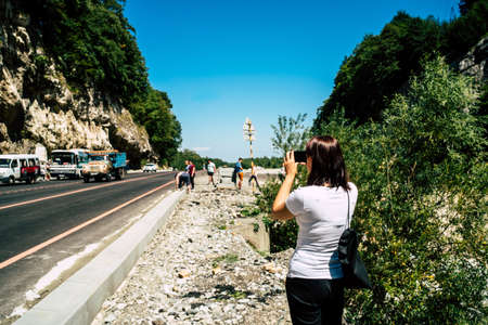 Young woman takes pictures of mountain landscape on smartphone. Female tourist photographing mountains on mobile phone.の写真素材
