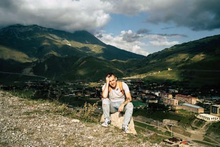 Tired traveling man resting on hill. Exhausted male tourist sitting on stone after active trekking in mountains.の写真素材