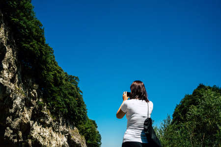 Young woman takes pictures of mountain landscape on smartphone. Female tourist photographing...