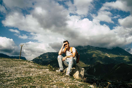 Tired traveling man resting on hill. Exhausted male tourist sitting on stone after active trekking in mountains.の写真素材
