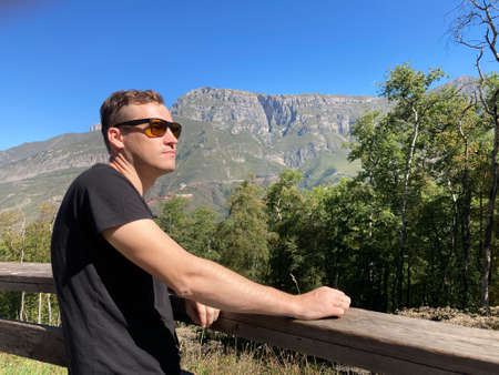 Young man in sunglasses stands on observation deck and looks away in sunny day. Male tourist enjoys...