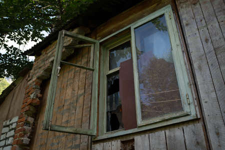 Window with broken glass in old building. Wooden window frame with partially broken glass in old abandoned wooden buildingの写真素材