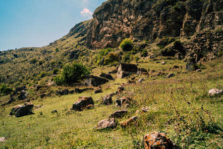 Ancient stone houses in green mountains. Amazing landscape with aged stone buildings located on green grassy slope of rocky mountain in sunny summer day.の写真素材
