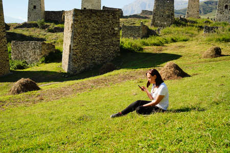 Carefree traveling woman relaxing on green lawn using smartphone. Serene female tourist with...
