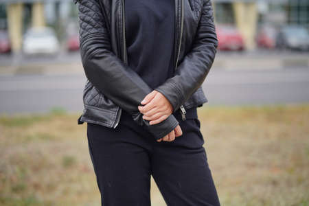 Close up of body part of female, standing on street in city. Body of unrecognizable woman in black casual clothesの写真素材