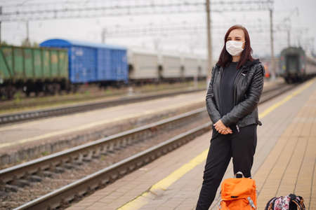 Woman in protective mask waiting for train on platform. Full length of female passenger in...