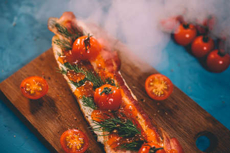Still-life of appetizing bruschetta on wooden board with steam. Close up of sandwich with melted cheese, bacon, cherry tomatoes, dill and sauce on blue backgroundの写真素材