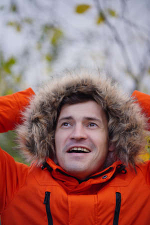 Portrait of adult man in hood and orange jacket enjoying nature in autumn season. Happy male enjoys...