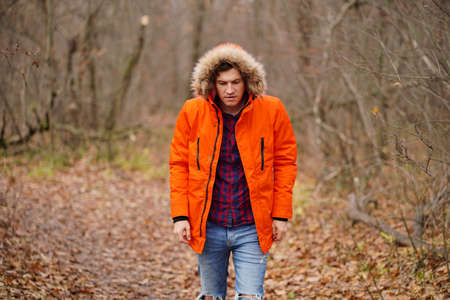 Young man in hood and orange jacket walking in autumn forest. Adult male on fresh air in autumn season.の写真素材