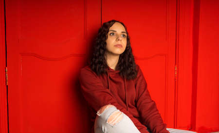 Young woman sitting on floor. Curly brunette poses near red wall.の写真素材