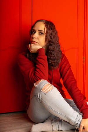 Young woman sitting on floor. Curly brunette poses near red wall.の写真素材