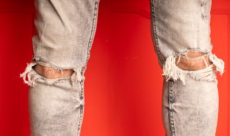 Close up of men's legs in jeans with holes on red background. Fashionable holes in gray jeans on unrecognizable manの写真素材