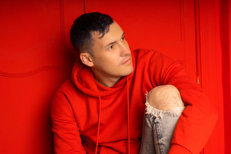 Young handsome male sitting on floor. Thoughtful man poses near red wallの写真素材