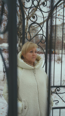 Portrait of adult woman standing in gazebo in park. Blonde posing through iron construction and looking away in winter seasonの写真素材