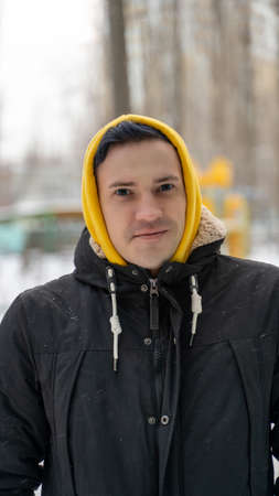 Portrait of young man in yellow hood on street in winter. Close up of adult male posing on walk in...