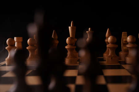 Close up of black chess pieces on board. Two rows of wooden figures on chessboard on black background. Concept of intelligent, logical and strategic game.の写真素材