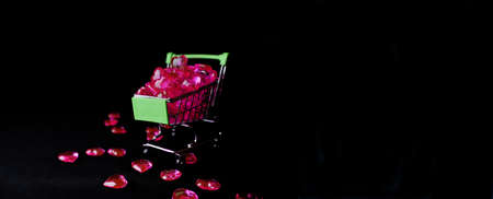 The red Heart shapes in shopping cart. A small supermarket cart full of red hearts on a black background. The concept of shopping in the supermarket, donation, charity.の写真素材
