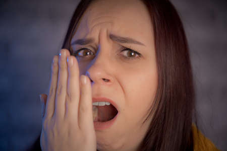 A yawning woman against background of gray brick wall. Young brunette covers her mouth and yawns in...