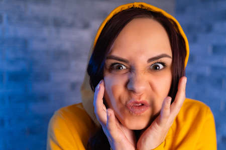 Portrait of young woman with grimacing face. Close up of crazy female in yellow hoodie monkeying on...