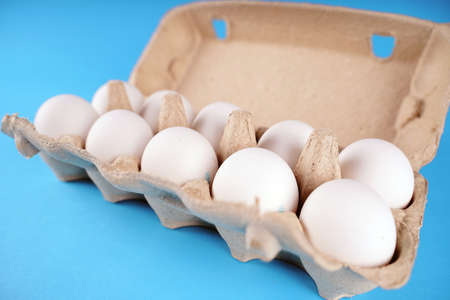 Farm raw, fresh white chicken egg in an egg box on a blue background. Eggs in carton. Eggs in the...