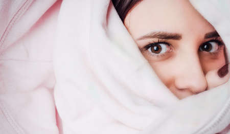 A woman looks out from under the blanket. Female hiding under a blanketの写真素材