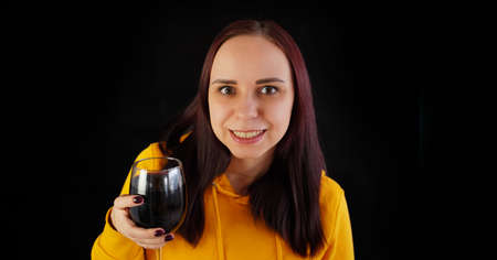 Relaxed young woman poses with glass of red wine on black background. Adult happy brunette resting with alcohol in her weekendの写真素材