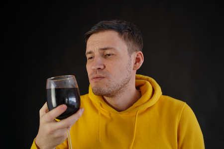 Relaxed young man poses with glass of red wine on black background. Adult happy guy resting with alcohol in his weekendの写真素材