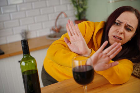 Unhappy young woman has headache from red wine. Adult female feels bad from alcohol while in kitchenの写真素材