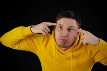 Portrait of young man in yellow hoodie with grimacing face. Close up of funny guy monkeying on black...