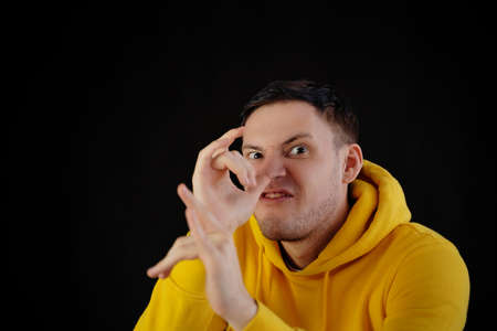 Portrait of young man in yellow hoodie with grimacing face. Close up of funny guy monkeying on black backgroundの写真素材