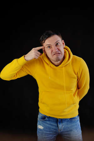 Portrait of young man in yellow hoodie with grimacing face. Close up of funny guy monkeying on black...
