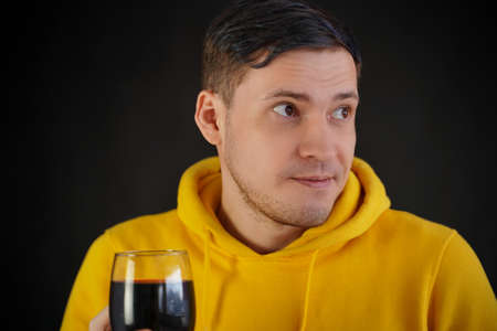 Relaxed young man poses with glass of red wine on black background. Adult happy guy resting with alcohol in his weekendの写真素材